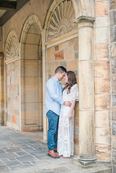 Engaged couple standing against stone building while touching their foreheads before their Wedding in Milwaukee.