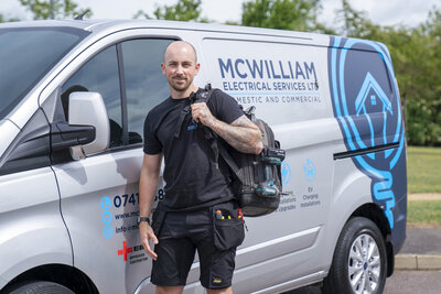Electrician stood in front of his work van holding tools