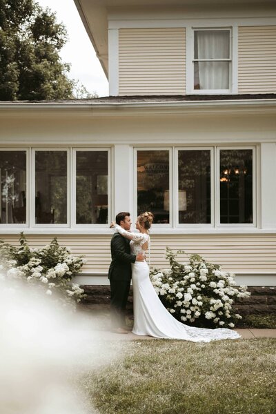 bride and groom embrace in front of their family home for a backyard wedding