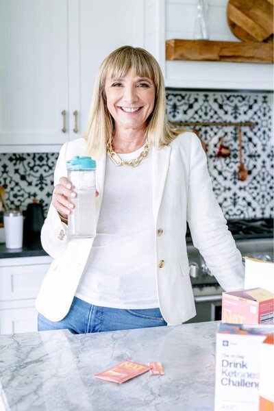 Female Health Coach holding a shake tumbler leaning against a counter with boxes of her products posing for a brand photo session.