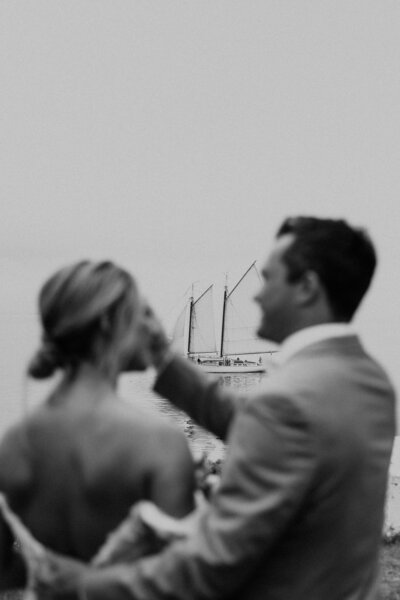 bride and groom looking at each other with sail boat in background