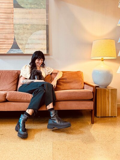 Salon owner Arianna sits on a couch with her pup, representing her warm, easy-going personality that makes her Eugene salon special.
