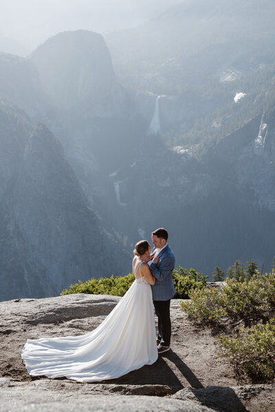 A newlywed couple with their arms around each other smiling at an overlook in Yosemite