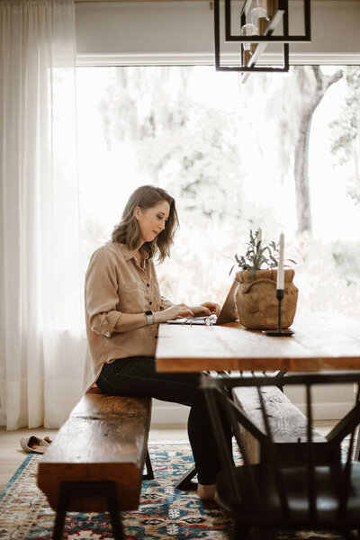 Woman sitting at a dining table, slightly smiling and looking at a laptop