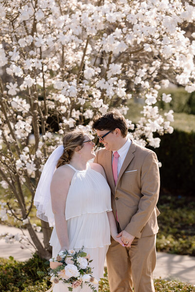 Bride and groom looking at each other in front of a blossoming tree in the spring.
