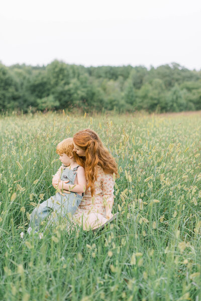 woman holding son in a tall grass field by Richmond Family photographer