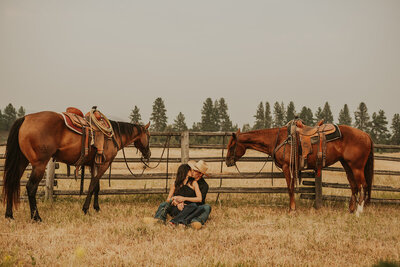 A couple kisses behind a cowboy hat while sitting on horses