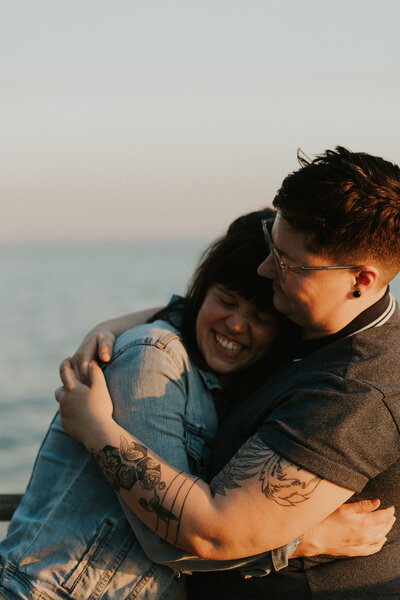 A couple hugging warmly with smiles by the water during sunset in Seattle.