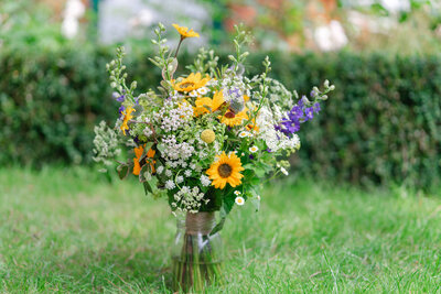 Colourful summer wedding bouquet with sunflowers, wildflowers, and greenery placed on grass
