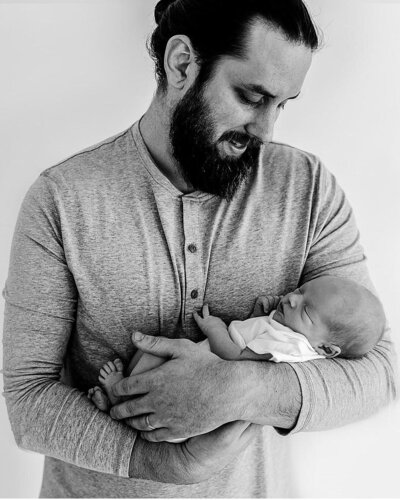 a black and white image of a family holding his newborn baby taken by Pensacola Portrait Studio Photographer Amanda Leatherberry