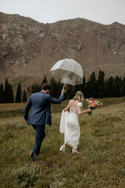 Man and woman walk through wildflower field during rainy wedding day.