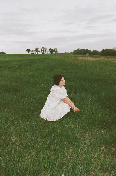 woman sitting alone in an open Kansas field wearing a white dress on a calm overcast day

