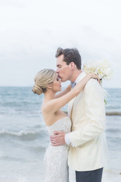 Groom kissing bride's forehead on beach
