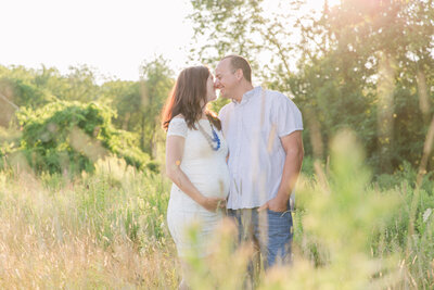 maternity couple in field kissing