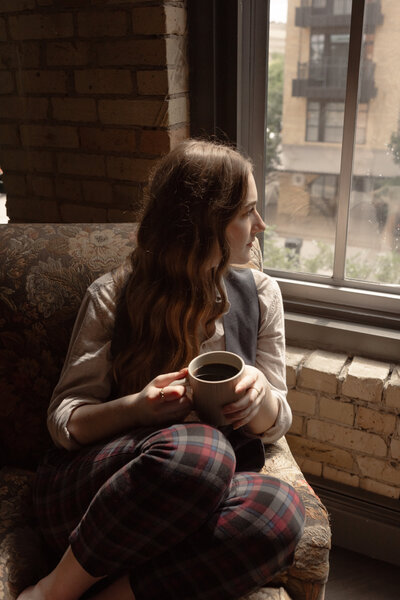Girl with dark blonde hair sitting in a chair looking out a window