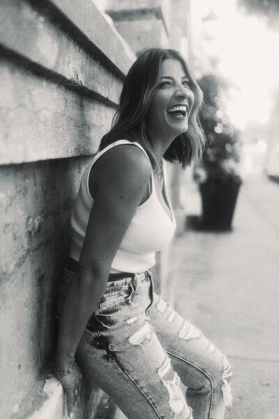 Black and white photo of woman laughing wearing white top and jeans