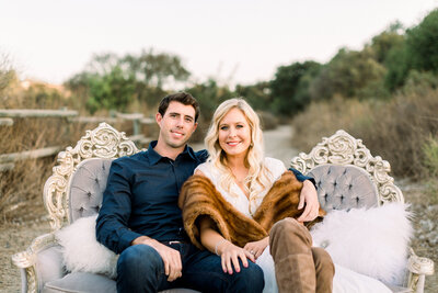 Engaged couple sit on a antique sofa in the middle of a walking trail at the Northwest Open Space