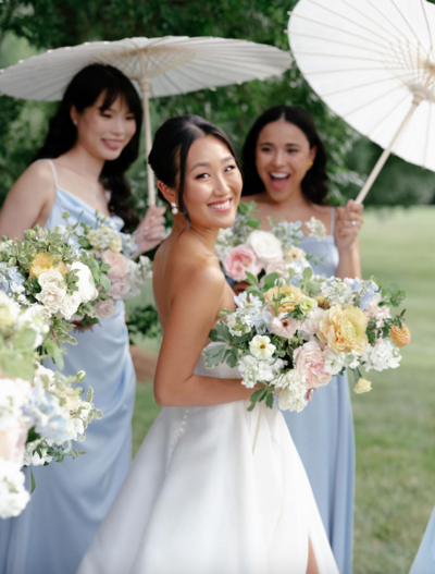 smiling bride and her bridesmaids holding spring florals in white and blue gowns at veritas winery