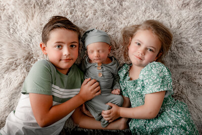 older brother and sister kiss and snuggle on their newborn baby brother