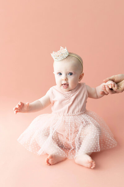 Minimalist digital illustration of a baby girl in a pink tutu and crown, seated on a soft blush background to celebrate a one-year milestone captured by duehr photography in minneapolis