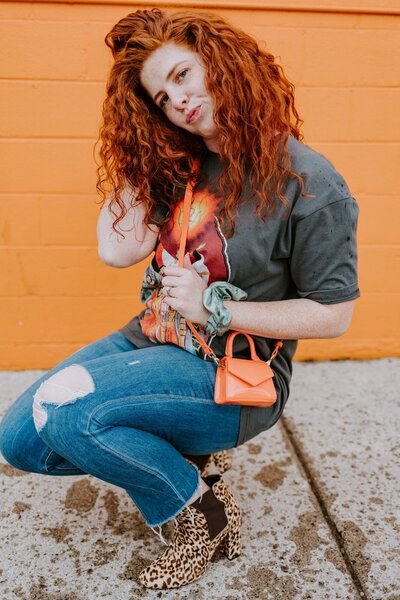 Leanna wear a bright orange purse and leopard print shoes while in front of a bright orange wall.