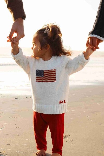A little girl joyfully holds hands with her parents while walking on the beach, captured by a family photographer.
