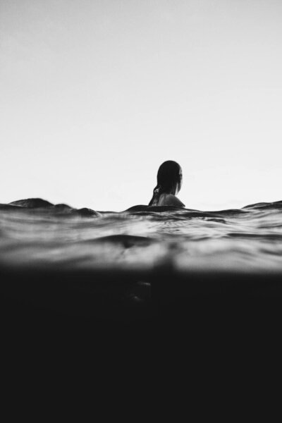Black-and-white image of a woman partially submerged in deep water, with the horizon in the background, emphasizing a serene and tranquil mood.