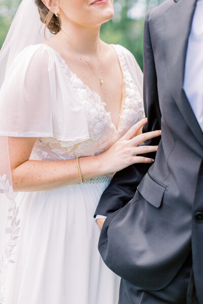 A bride in a flowing wedding dress stands gracefully by a large window, bathed in natural light.