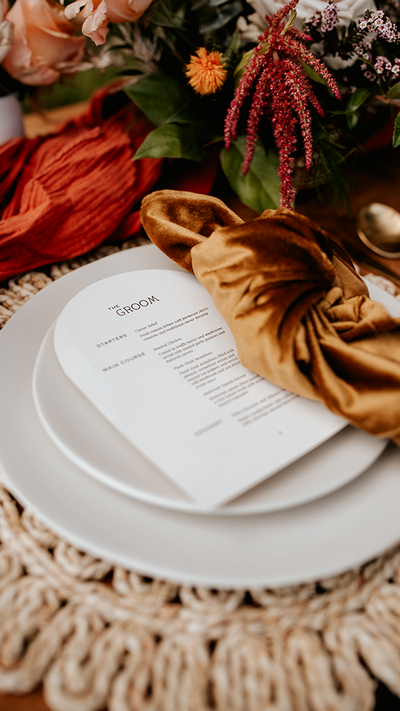 White menu card on a plate with a brown velvet napkin and flowers