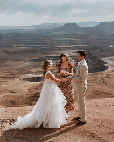 bride and groom standing with their officiant getting married to each other in the desert
