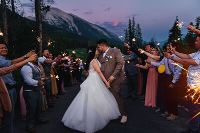 Bride and groom standing in the middle of guests holding sparklers at twiglight.