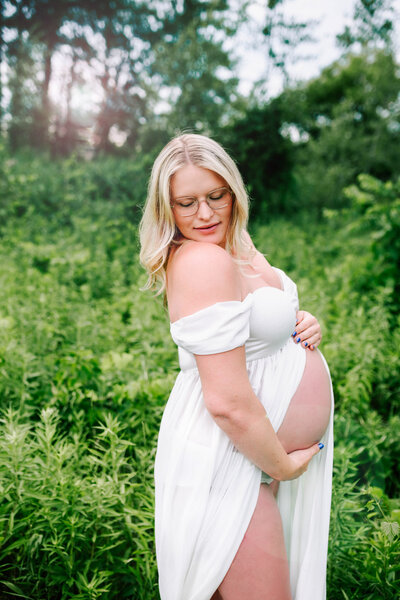 expecting mother in white dress with her belly showing in standing in a green field.