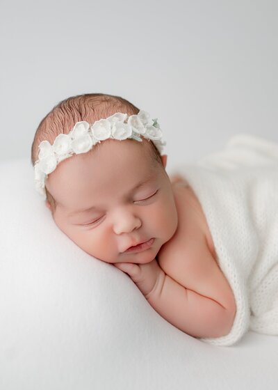 newborn baby girl lying on a white blanket wearing a flower headband