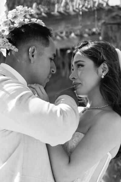 Black-and-white photo of groom wiping a happy tear from bride's cheek after their first look during their destination wedding in Mexico.