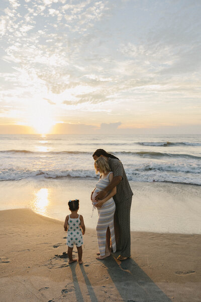 family maternity session on the beach with their child at sunrise.
