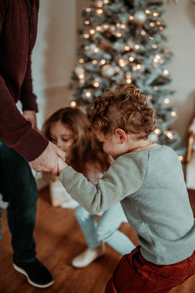 Family dancing around the Christmas tree at Evermore Place for a holiday card session in Gray, Maine.