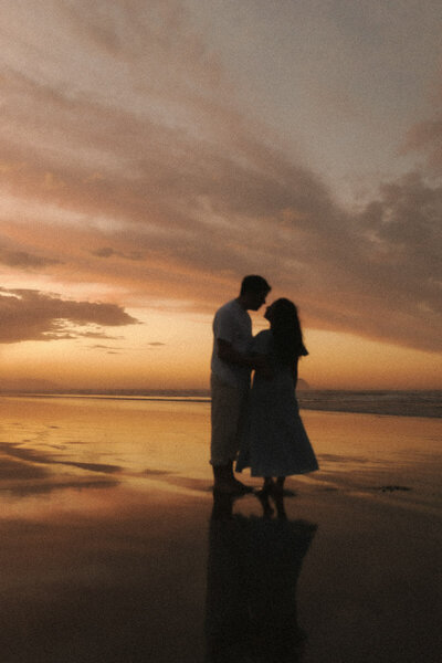 A vintage portrait of a couple at the Ohope beach holding each other at sunset. Captured by Eilish Burt Photography