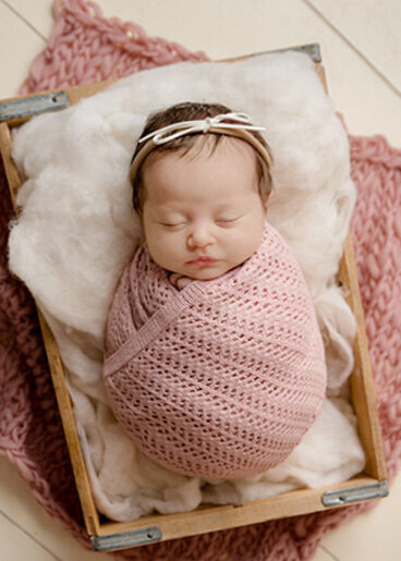 Swaddled baby girl wearing pink with a white bow headband.