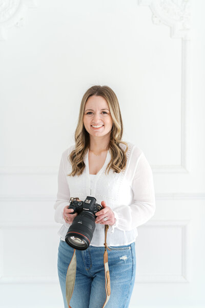Woman sitting on stool holding a camera and smiling