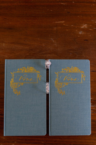 Wedding rings rest between two teal vow books