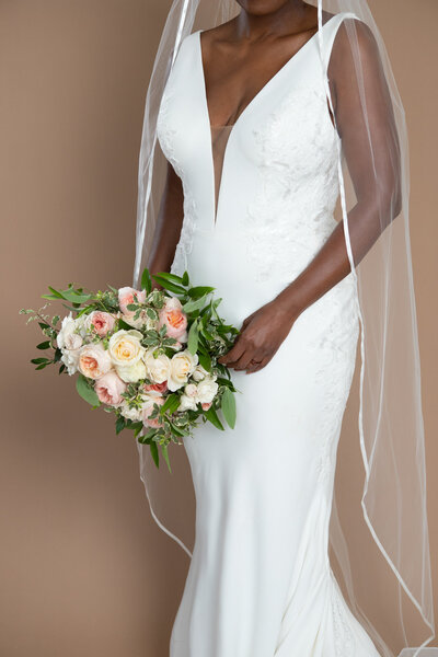 Bride wearing a floor length veil with ribbon edge and holding a white and blush bouquet