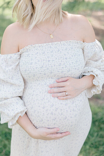 Pregnant mother in a cream floral dress holds her baby belly outside, Indianapolis Photographer