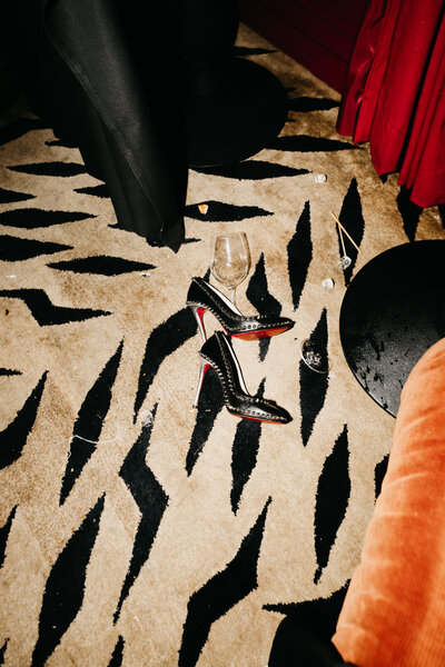 Black high heels and champagne glass on patterned carpet after wedding celebration