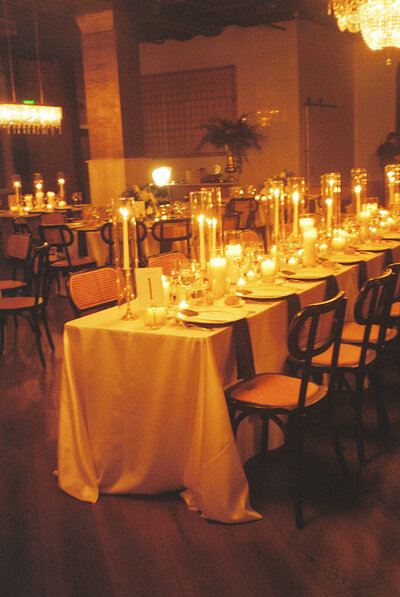 A warmly lit wedding reception table adorned with elegant candles, fine dinnerware, and soft linens, creating an intimate and cinematic ambiance.