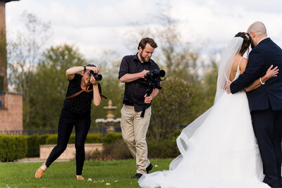 Sam & Grace take wedding photo and video with cameras on a grassy field in front of club corazon