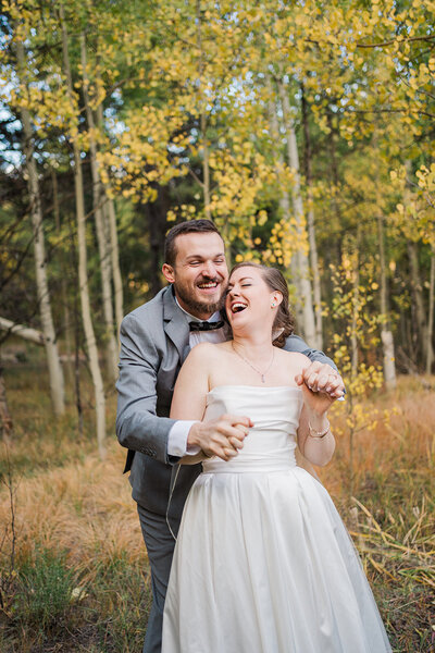 The groom hugs the bride while they laugh in a fall aspen forest in Breckenridge