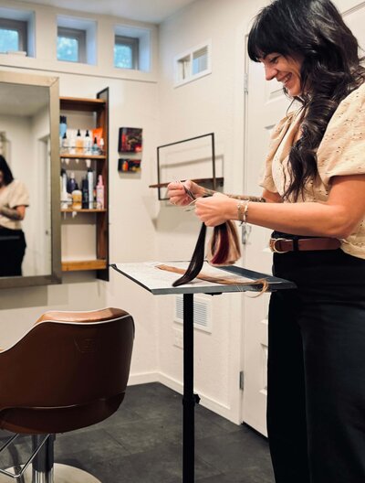 Hair stylist smiles while looking at hair extensions, representing her love for boosting her client's confidence.