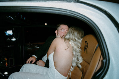 Bride grabbing grooms face and kissing him in a limo at the end of the night