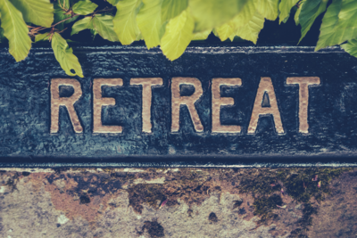 Close-up of a weathered stone sign with the word 'RETREAT' carved into it, framed by greenery