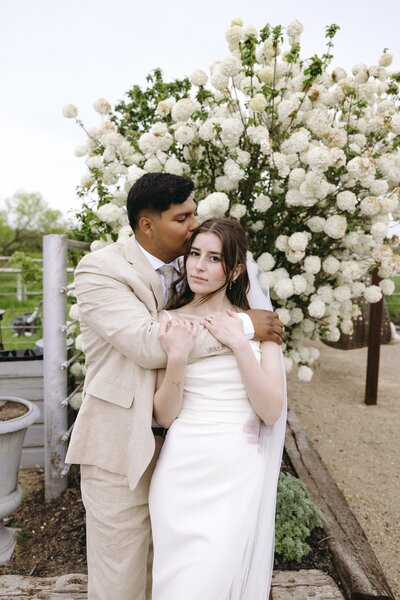 Romantic spring wedding portrait of a stylish couple embracing under blooming florals, captured by editorial wedding photographer Madison